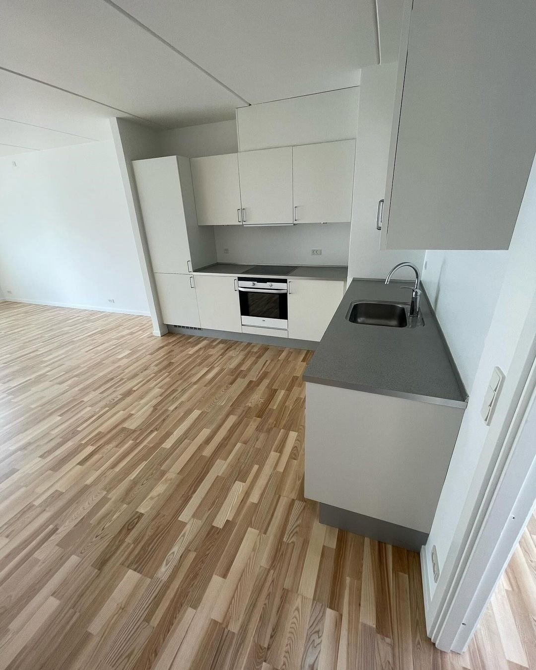 Lys moderne køkken med hvide skabe, trægulv og vask.