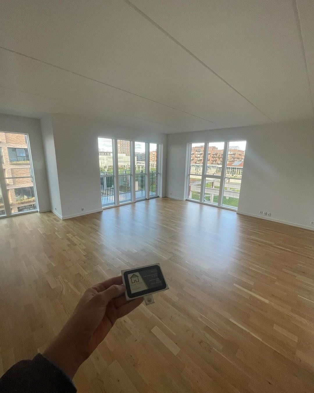 Lejlighed med store vinduer og lyst trægulv, klar til indretning.